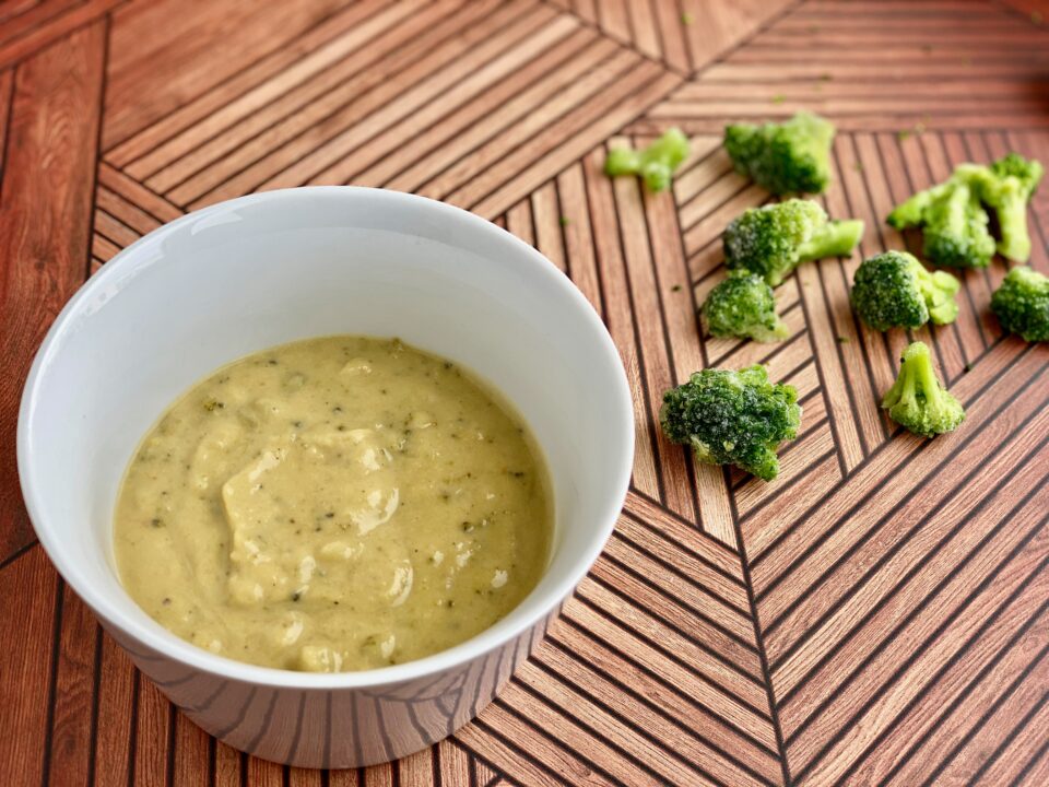 Image of a bowl of soup with pieces of broccoli in the background