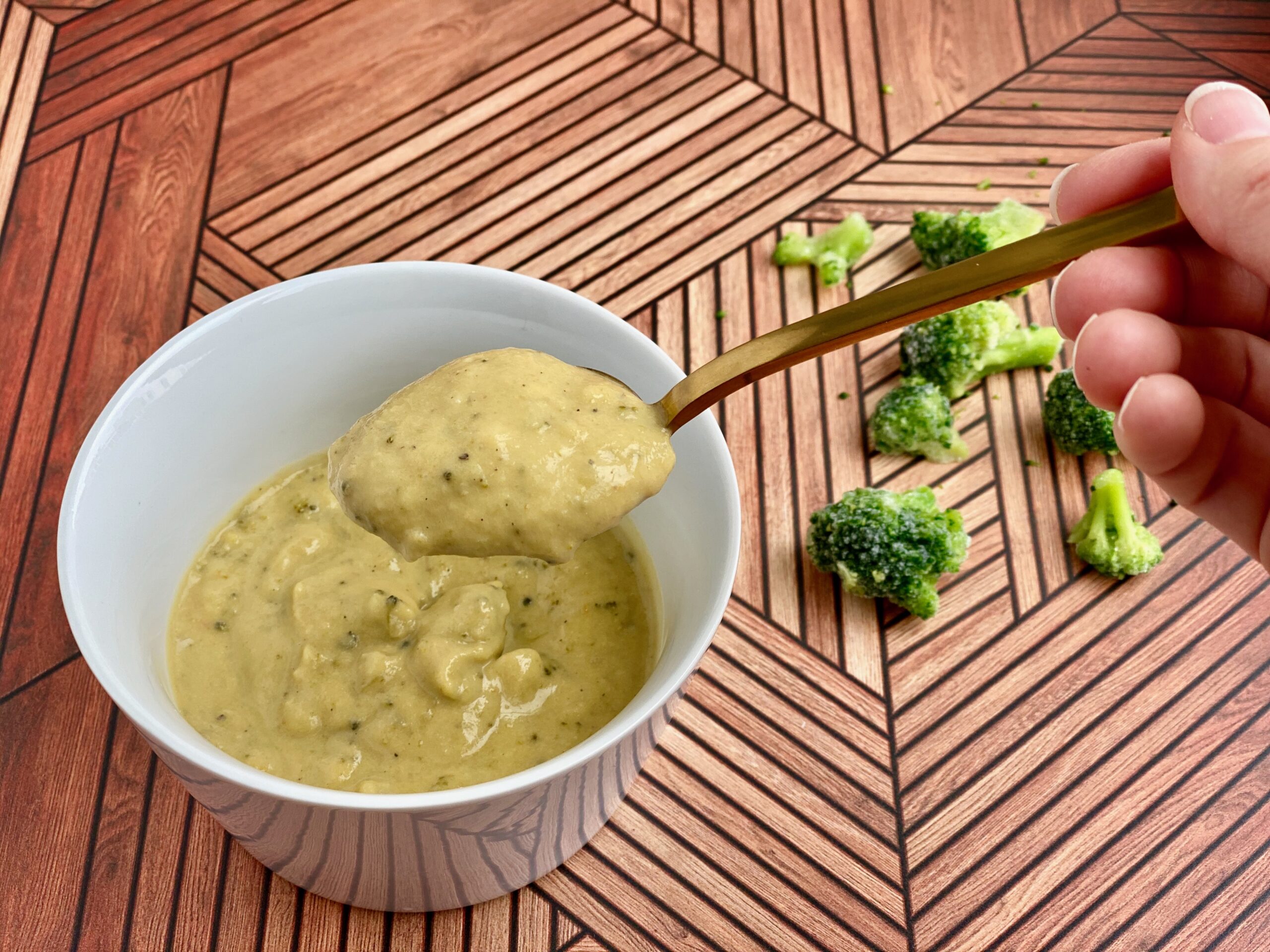 Easy Broccoli Cheddar Soup Image of a bowl of soup with a bite on a spoon and broccoli in the background