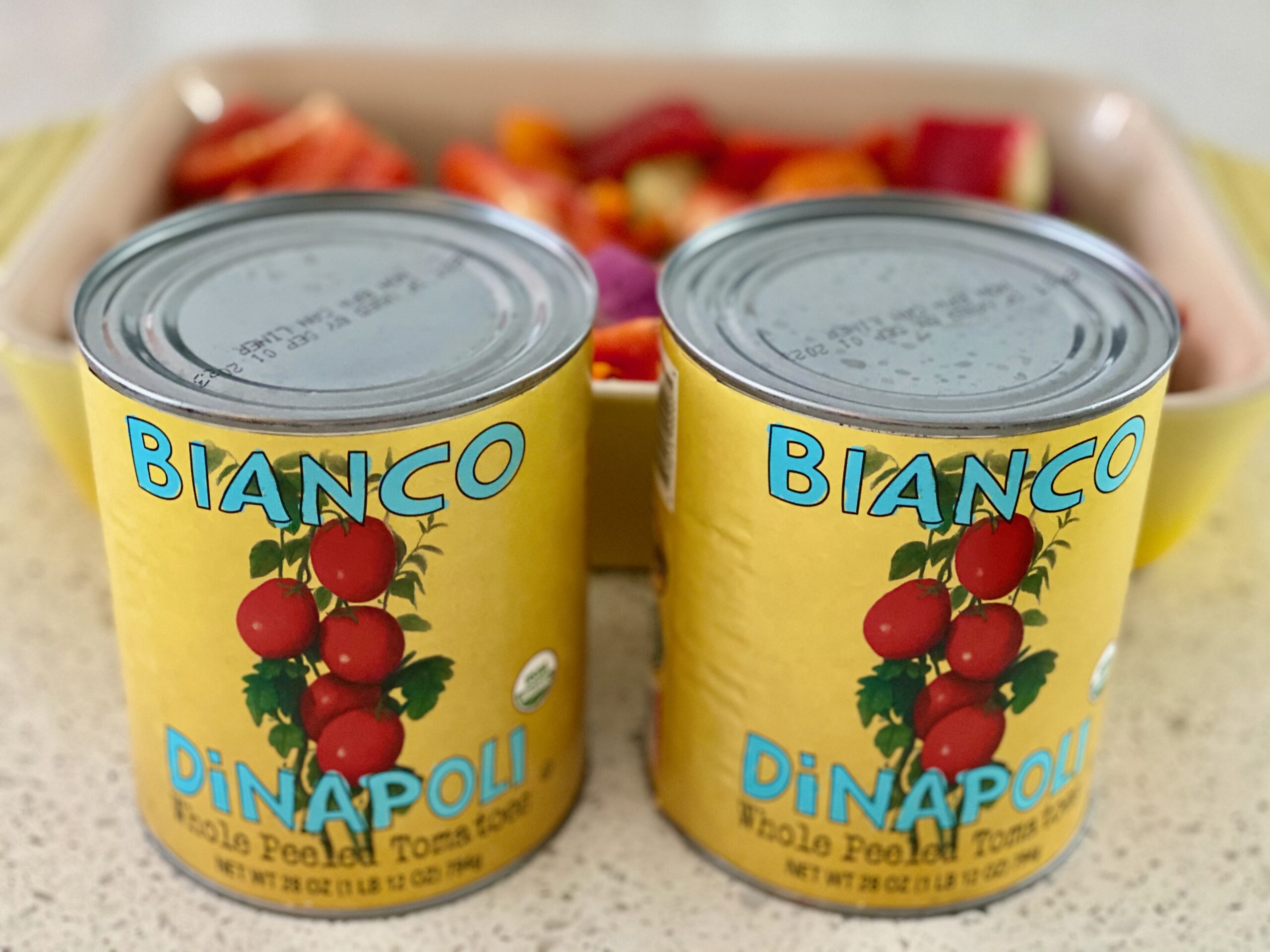 Easy Roasted Tomato Vegetable Soup An image of two cans of tomatoes with a pan of vegetables in the background