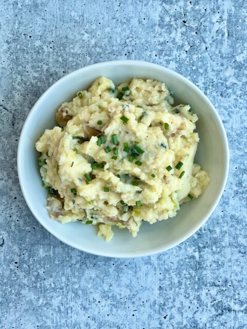 A bowl of smashed potatoes with green garlic